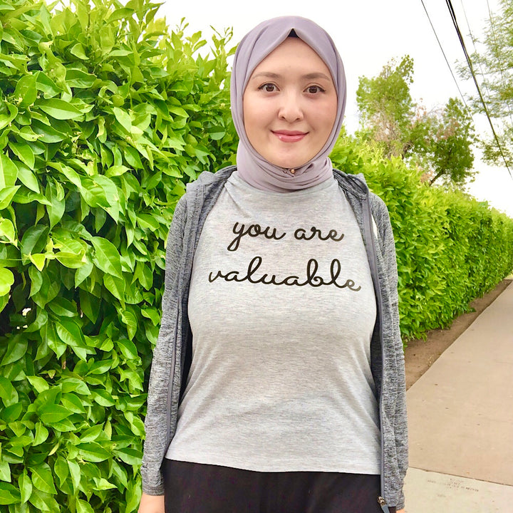 Woman wearing a grey muscle tank top that says "you are valuable"