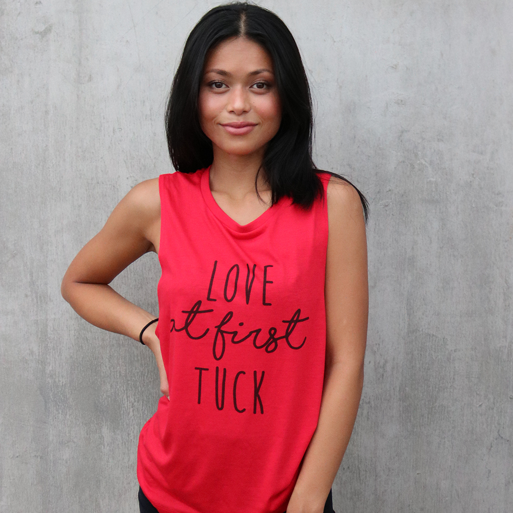 Woman wearing a red muscle tank top that says "love at first tuck"