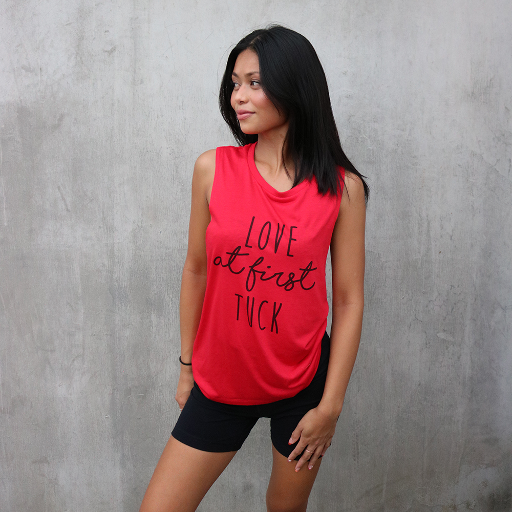 Woman wearing a red muscle tank top that says "love at first tuck"