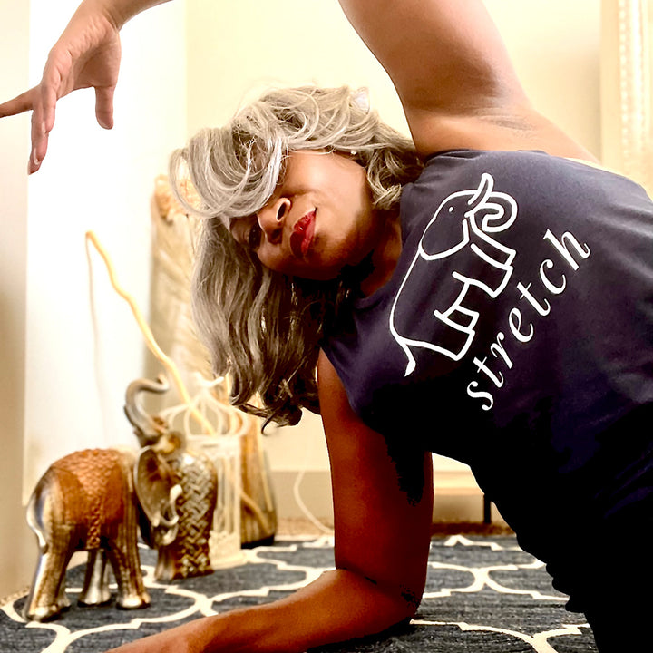 Woman wearing a blue muscle tank top from The Movement Shop that has an elephant and the word "stretch" on it