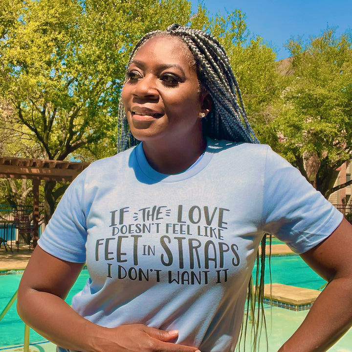 Woman wearing a unisex t-shirt that says "If the love doesn't feel like feet in straps, I don't want it". T-Shirt is from The Movement Shop.