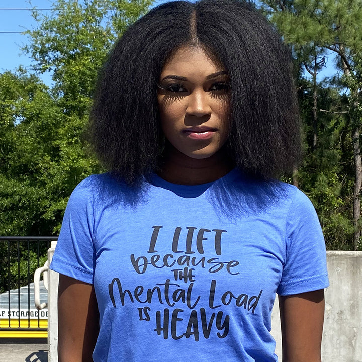 Woman wearing a heather columbia blue unisex t-shirt from The Movement Shop that says "I lift because the mental load is heavy".