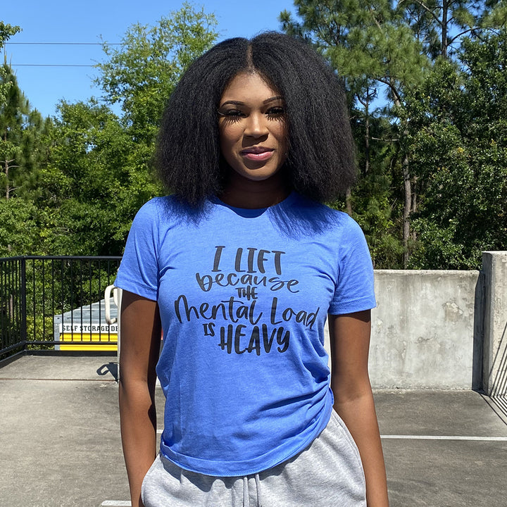 Woman wearing a heather columbia blue unisex t-shirt from The Movement Shop that says "I lift because the mental load is heavy".