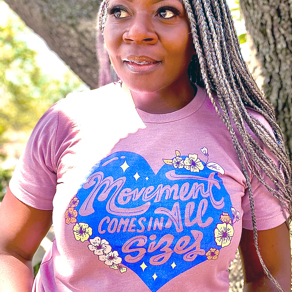 Woman wearing a unisex heather orchid t-shirt from The Movement Shop that says "Movement Comes In All Sizes" 