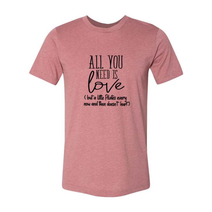 A heather mauve unisex crewneck t-shirt that says "all you need is love" but a little Pilates every now and then doesn't hurt"