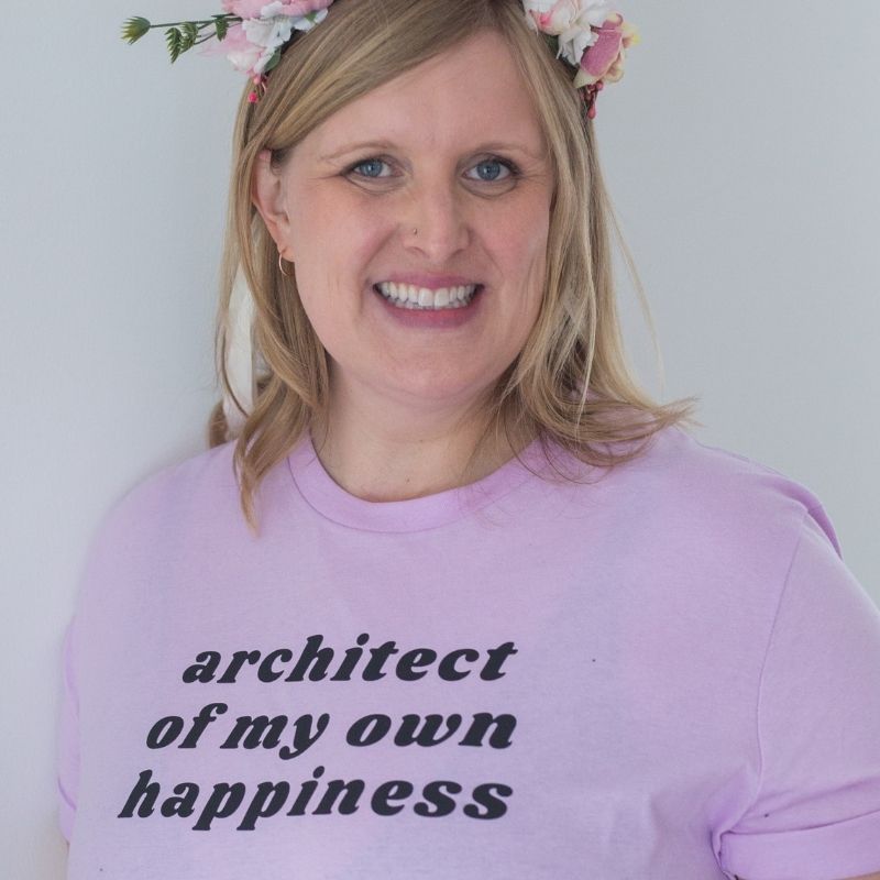 Woman wearing a heather prism lilac shirt that says "architect of my own happiness" in black font. Woman wearing a flower crown.