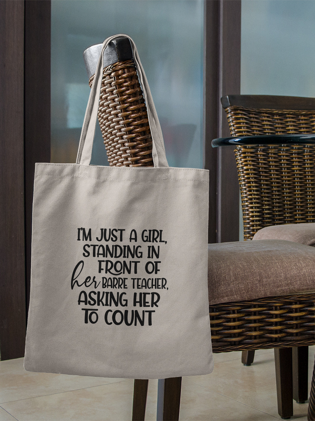 100% cotton canvas tote bag with handles that says "I'm just a girl, standing in front of her Barre Teacher, asking her to count". Bag is hanging off the back a wicker dining room chair. 