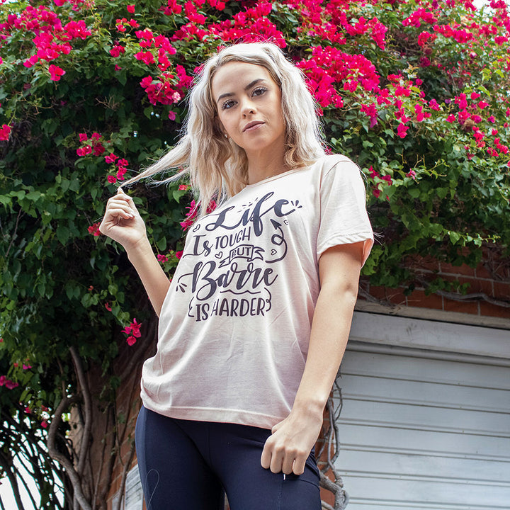 Woman wearing a heather peach unisex crew-t-shirt that says "Life is Tough But Barre Is Harder".