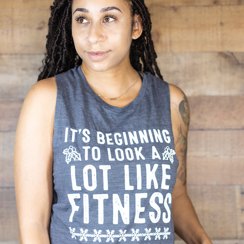 Woman wearing a grey muscle tank top that says " It's beginning to look a lot like fitness"