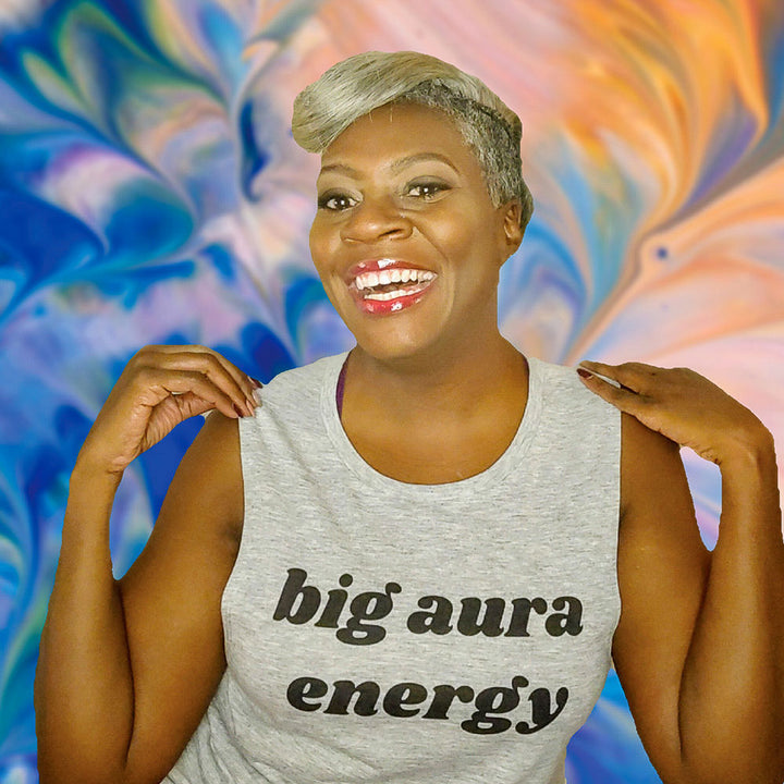 Woman wearing a grey muscle tank top that says "big aura energy" across the chest in black text.