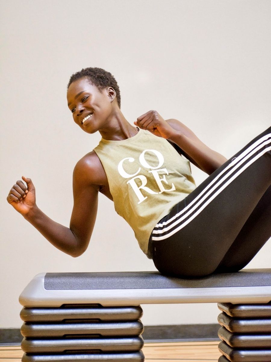 A woman wearing a heather olive muscle tank that says CORE in white text in front.