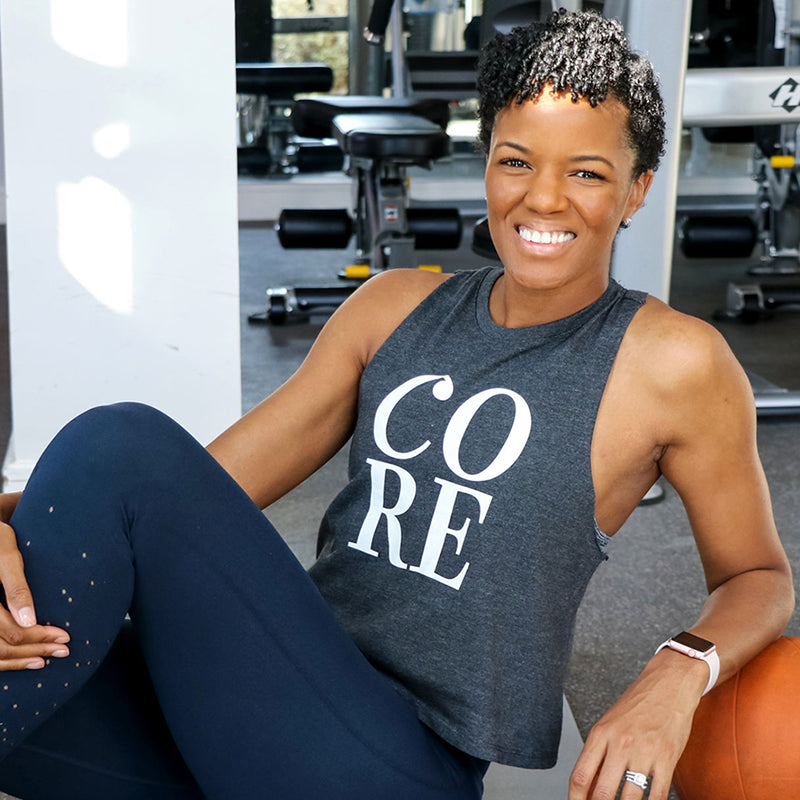 A woman wearing a dark heather gray muscle tank that says CORE in white text in front.