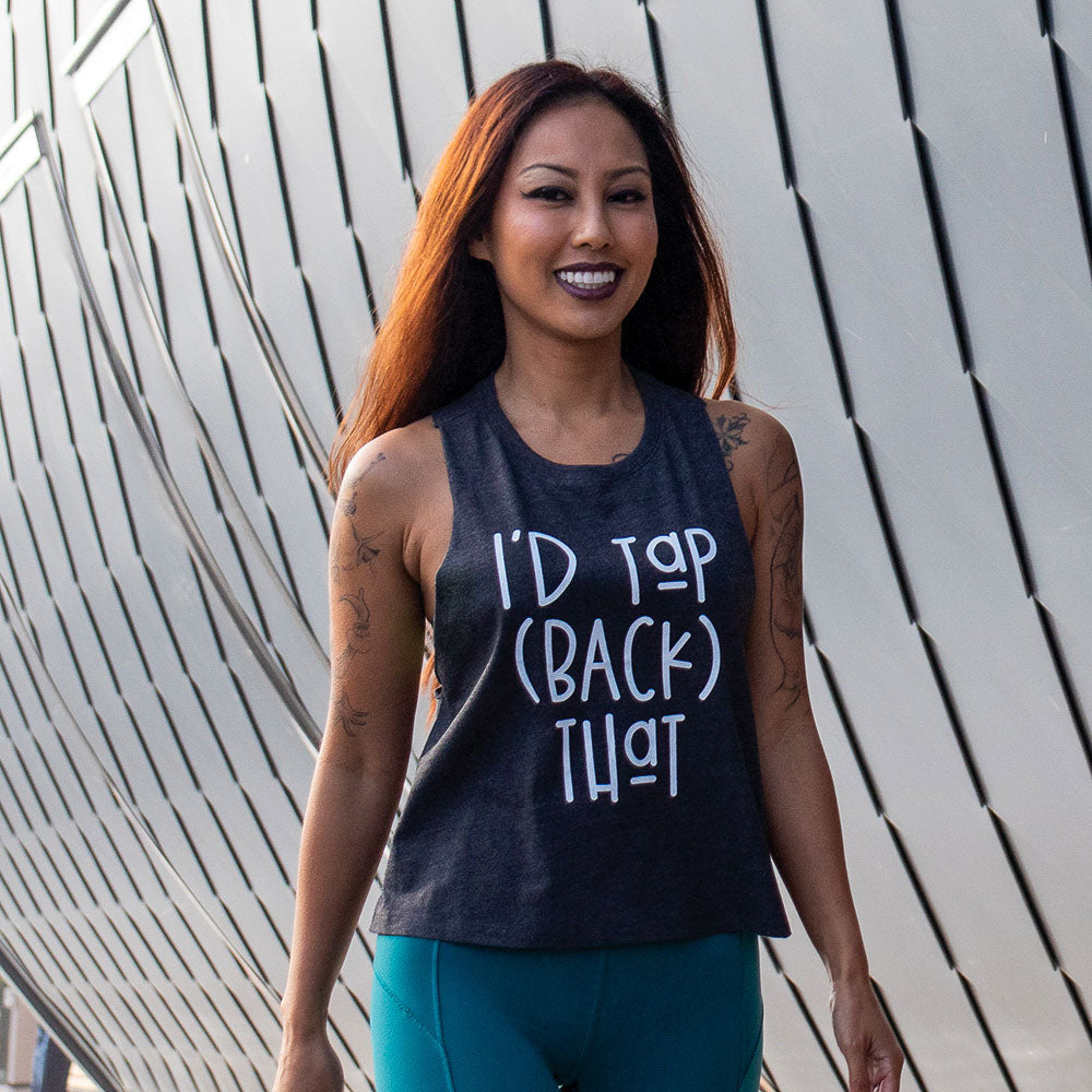Woman wearing a cropped muscle tank top that is dark grey heather and says "I'd Tap (Back) That" in white text