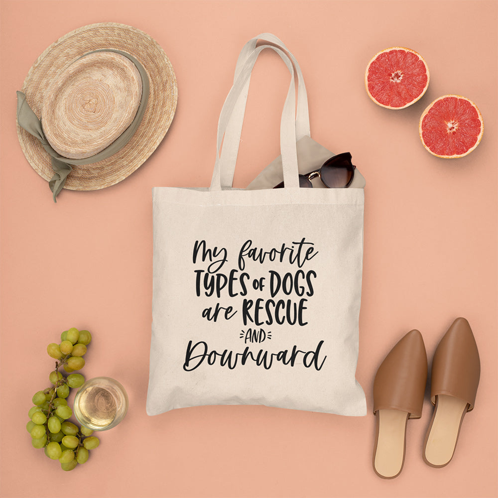 Canvas tote bag that says "my favorite types of dogs are rescue and downward". Tote is lying a coral color flat lay