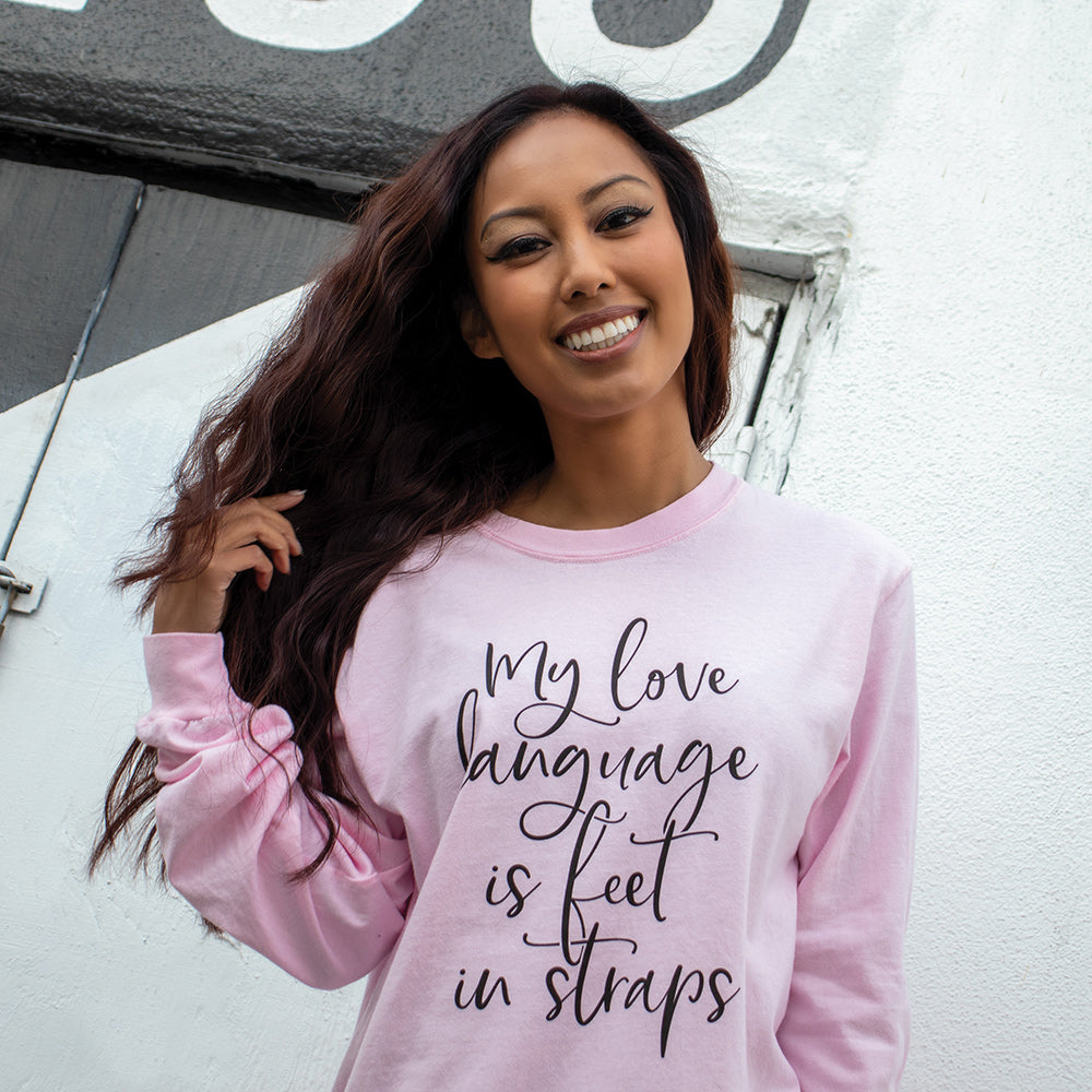 Woman wearing a unisex crew neck long sleeved shirt that says "My Love Language Is Feet In Straps" in black script