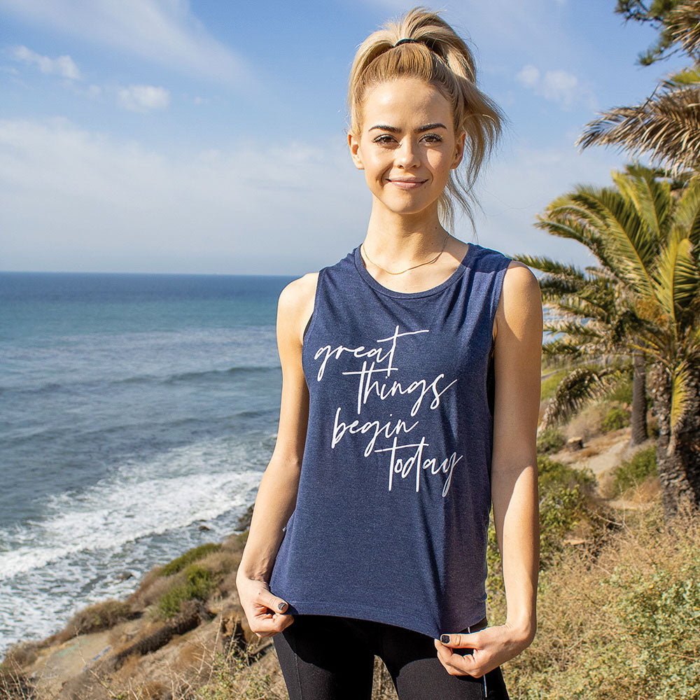 Woman wearing a blue muscle tank top that says "great things begin today" in white script