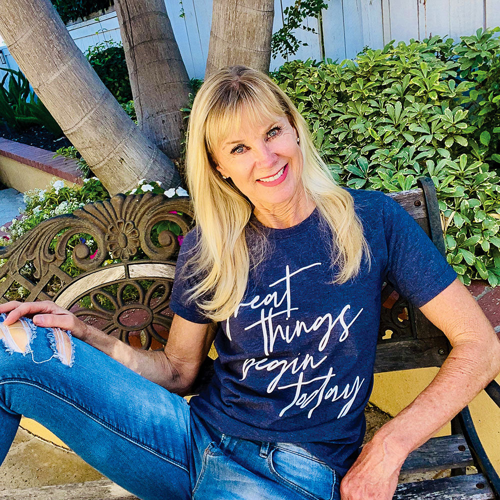 Woman wearing a unisex crewneck heather navy t-shirt that says "great things begin today"  in white script text