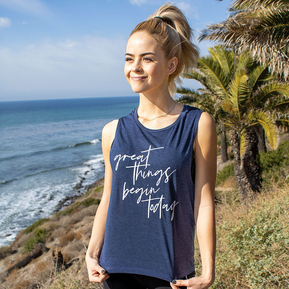 Woman wearing a blue muscle tank top that says "great things begin today" in white script