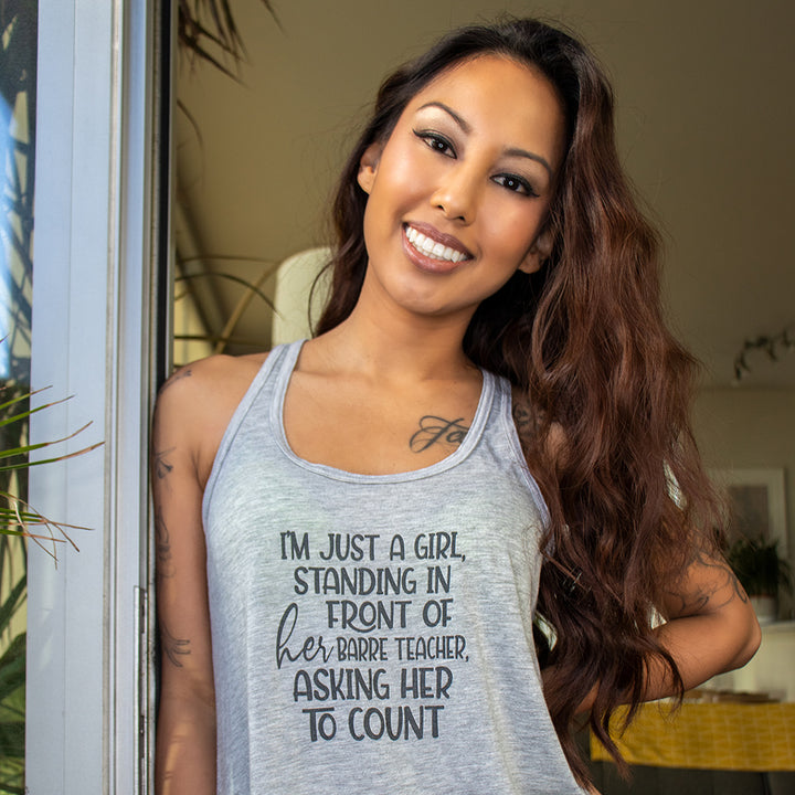 Women wearing a grey racerback tank top that says "i'm just a girl, standing in front of her barre teacher, asking her to count"