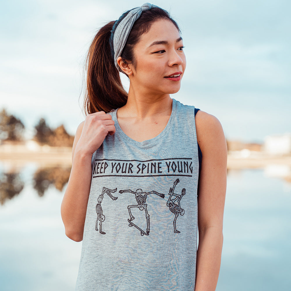 woman wearing a grey muscle tank top with skeletons dancing that says "keep your spine young"