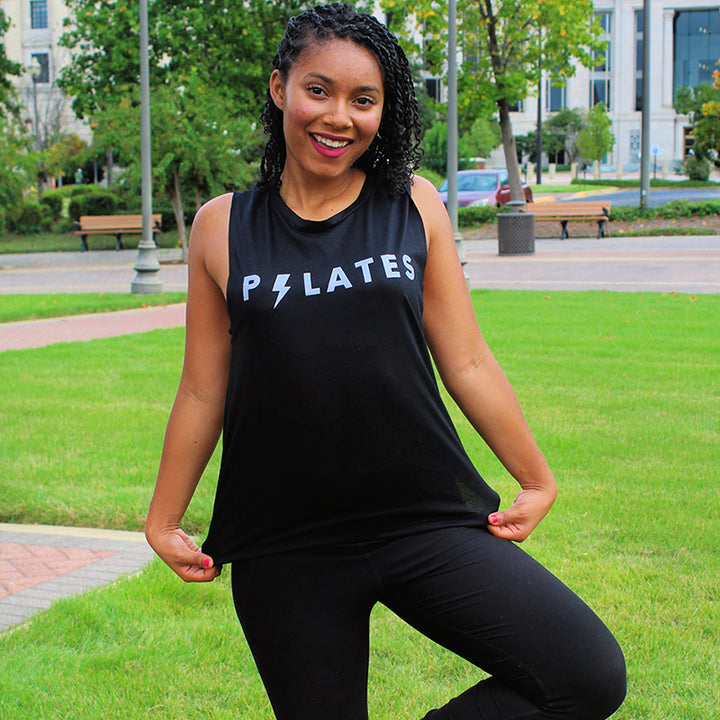 Woman wearing a black muscle tank top that says "Pilates". The 'I' in Pilates is shaped like a lightening bolt.