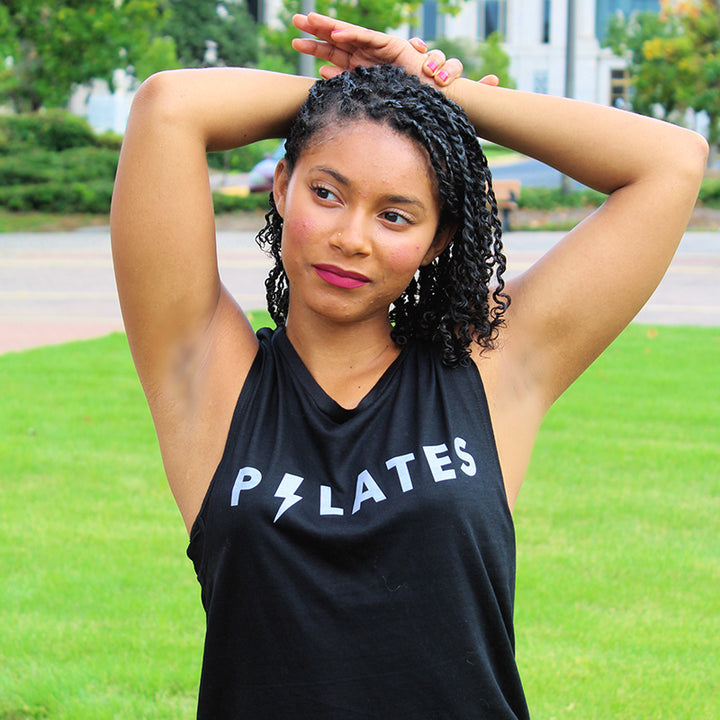Woman wearing a black muscle tank top that says "Pilates". The 'I' in Pilates is shaped like a lightening bolt.