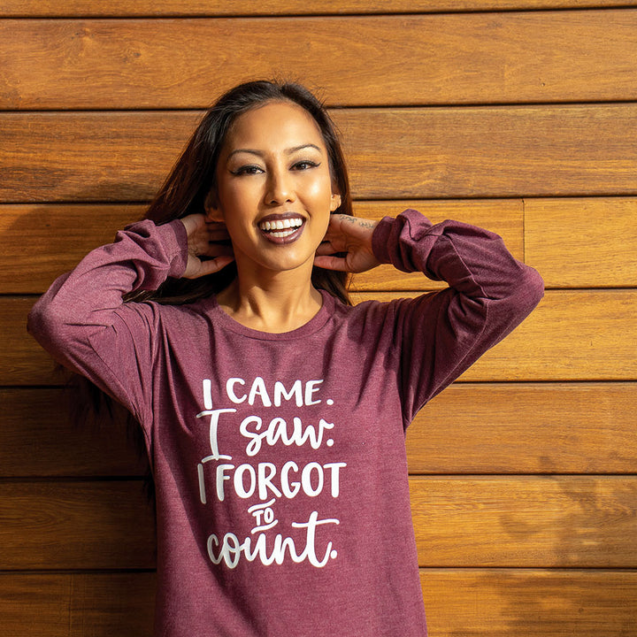 Woman wearing a maroon triblend unisex long sleeve crew neck shirt that says "I came. I saw. I forgot to count." in white bold text. 