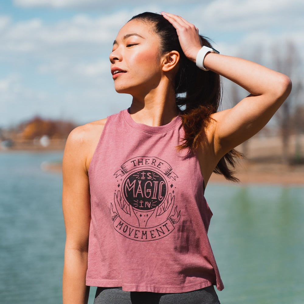 Woman wearing a mauve racerback tank top that that says "There is Magic In Movement" with a crystal bar design 