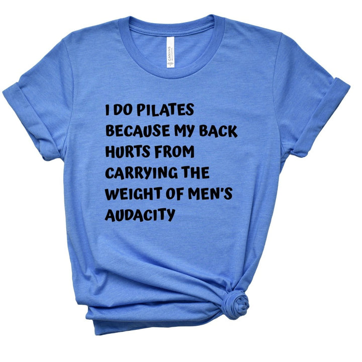 A heather columbia blue t-shirt that says "I do Pilates because my back hurts from carrying the weight of men's audacity". T-Shirt is from The Movement Shop