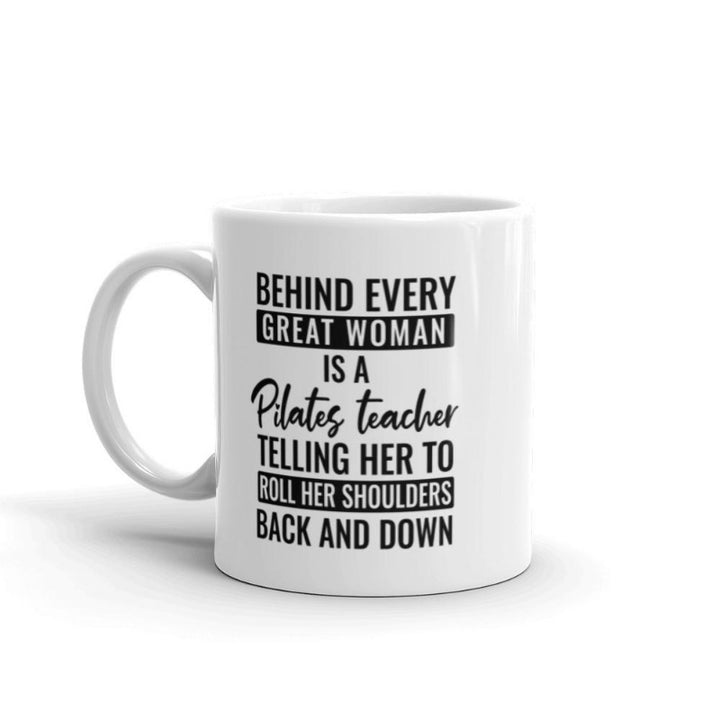 11 oz coffee mug that says "Behind Every Great Woman is A Pilates Teacher telling her to roll her shoulders back and down"