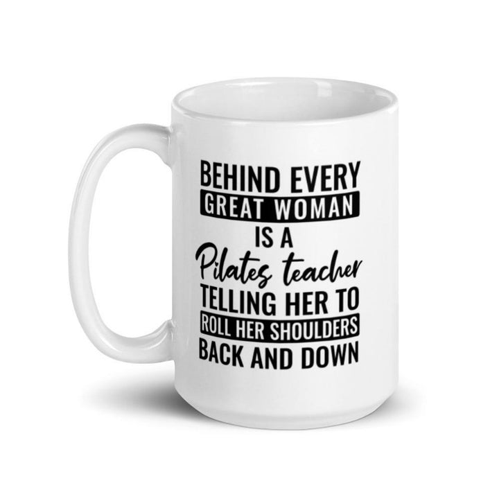 15 oz coffee mug that says "Behind Every Great Woman is A Pilates Teacher telling her to roll her shoulders back and down"