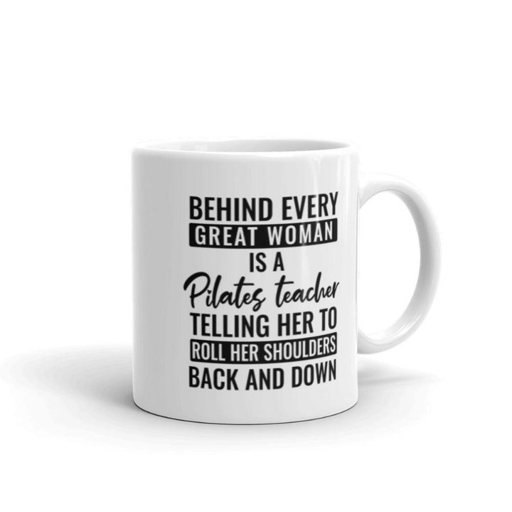 11oz coffee mug that says "Behind Every Great Woman is A Pilates Teacher telling her to roll her shoulders back and down"