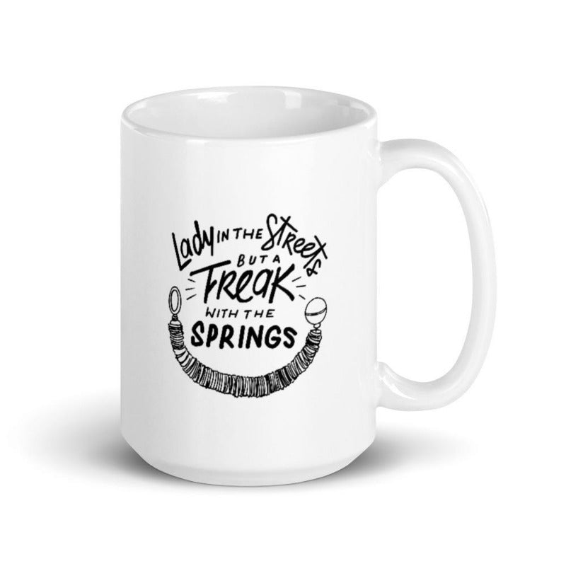 15oz Coffee Mug that says Lady In The Streets But A  Freak With The Springs. There is Pilates reformer spring under the text. Design is in black.