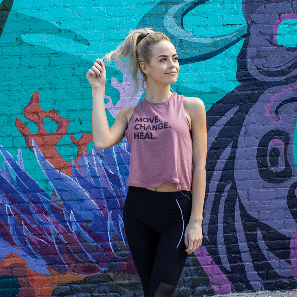 Woman wearing a mauve crop muscle tank top that says "Move. Change. Heal." in black text 