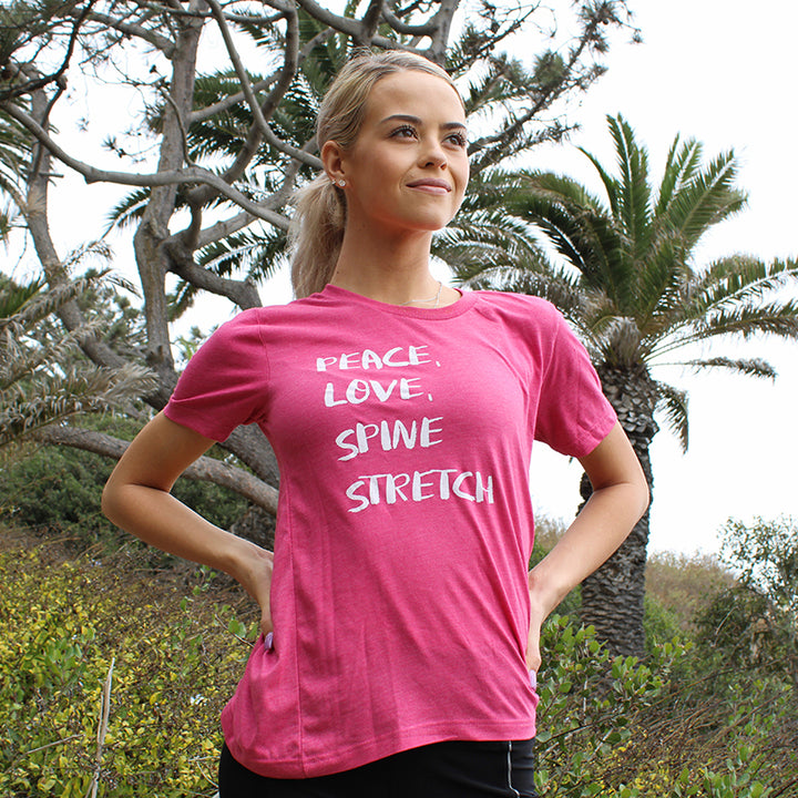 Woman wearing a Heather Raspberry Unisex Crewneck T-Shirt Peace, Love, Spine Stretch. Trees are in the background.