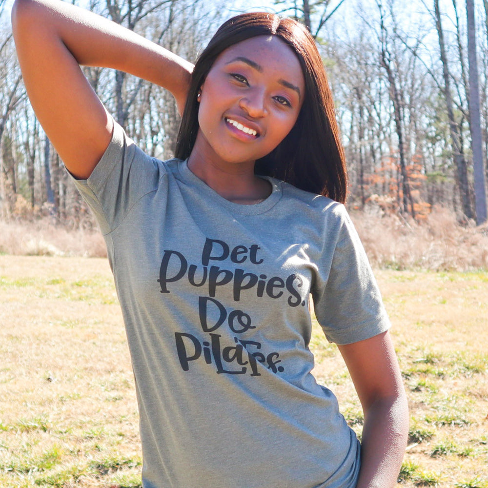 Woman wearing a unisex crewneck green t-shirt that says "Pet Puppies, Do Pilates" in black text
