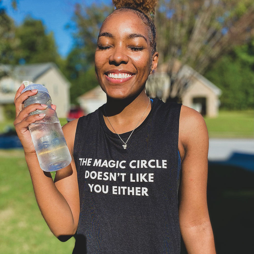 Woman wearing a black muscle tank top that says "The Magic Circle Doesn't like you either" in white all caps text.