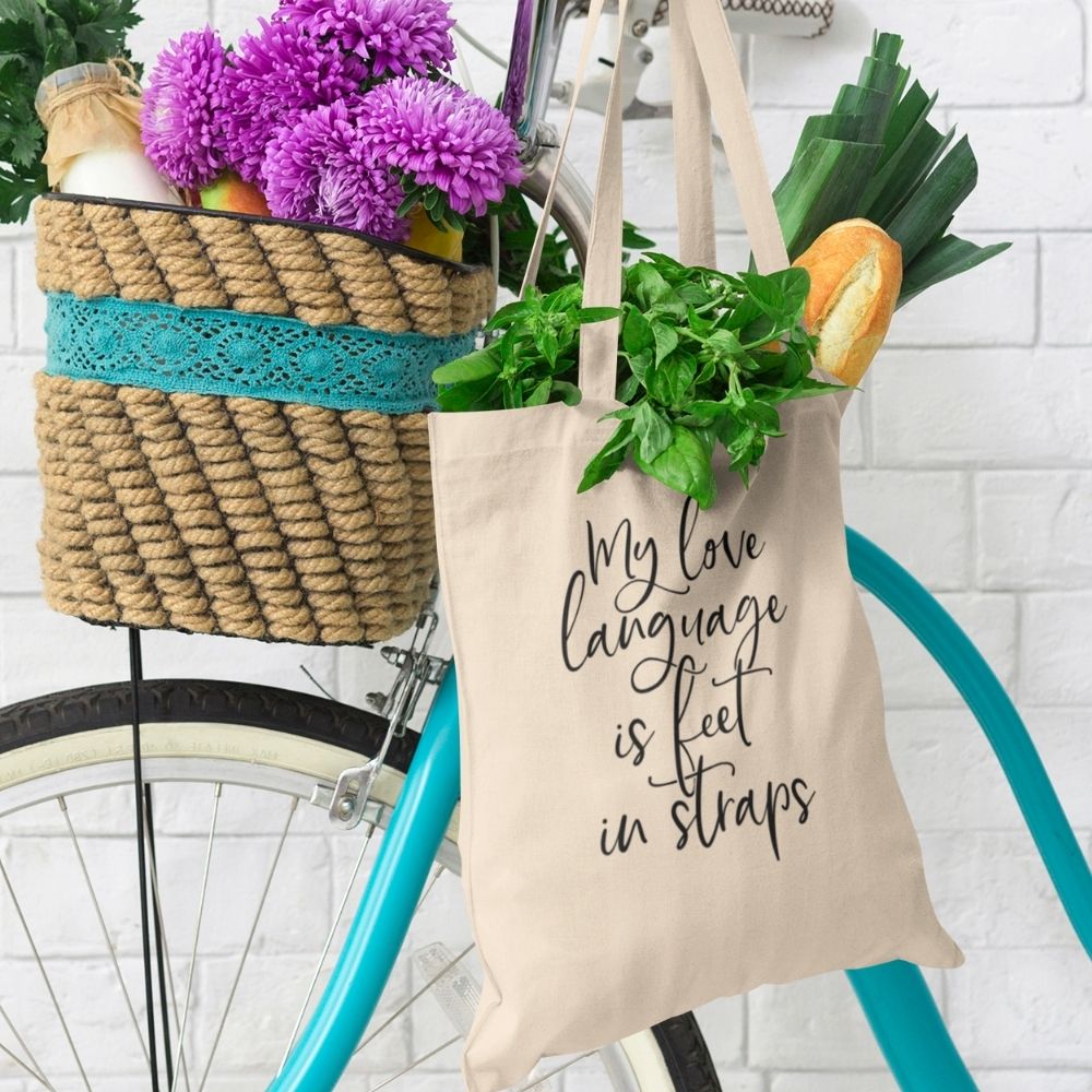 Pilates Canvas Tote bag hanging off a bike handle. Tote bag says "My Love Language Is Feet In Straps" in black text