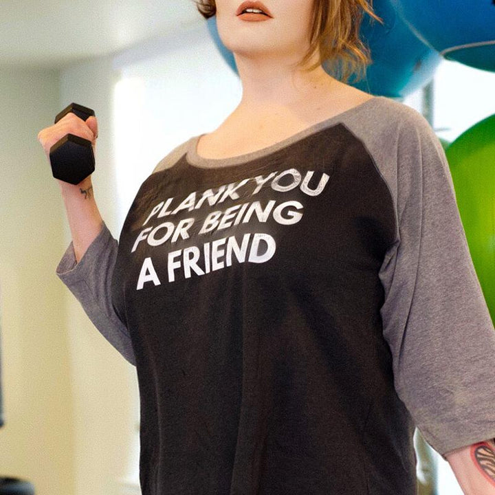 Woman wearing a 3/4 sleeve baseball shirt that says "Plank You For Being A Friend"