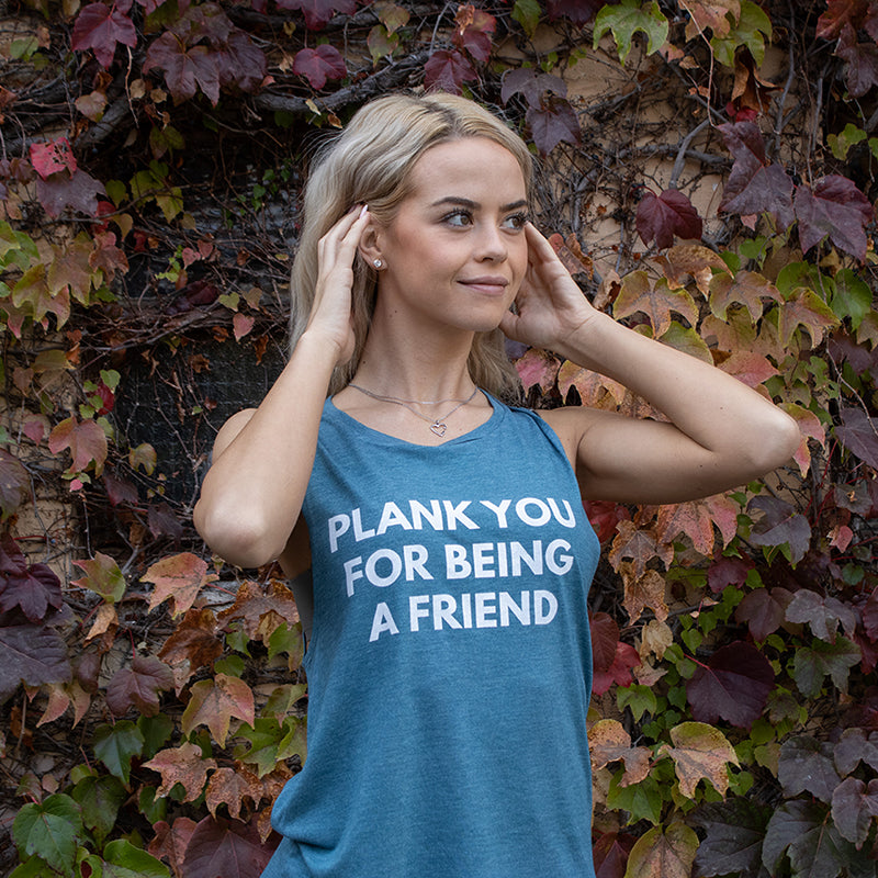Woman wearing a teal muscle tank top that says "Plank You For Being A Friend" in white text.