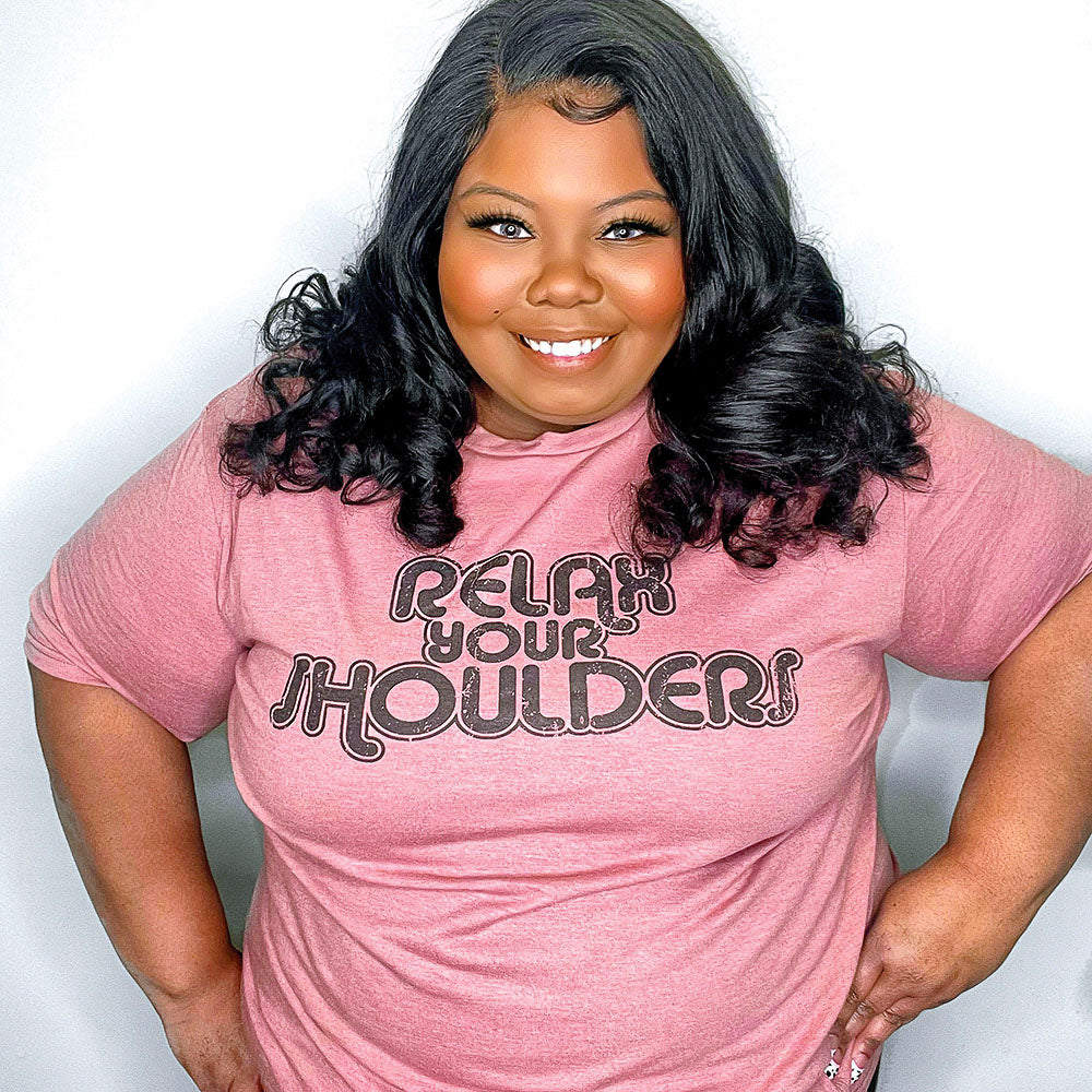 Woman wearing a heather mauve crewneck t-shirt that says "Relax Your Shoulders" in vintage retro text