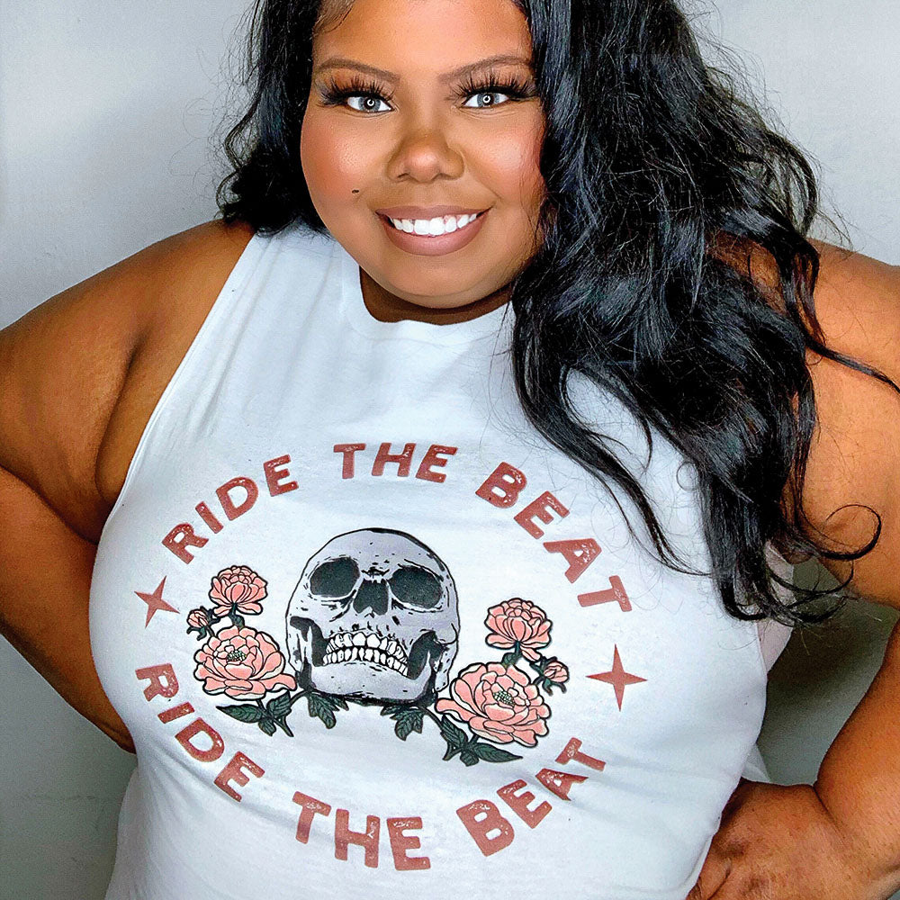 Woman wearing a white tank top that says "ride the beat" with a skull in the middle 