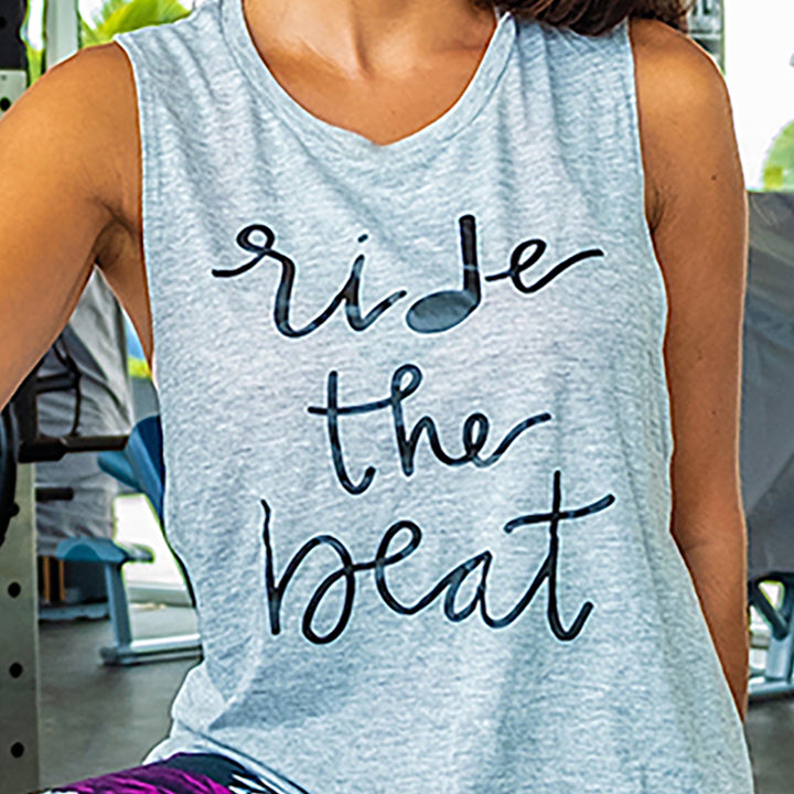 Woman wearing a grey tank top that says "ride the beat" in black text. 