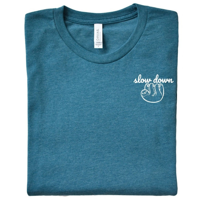 Folded Heather Deep Teal Unisex Crewneck T-Shirt that has the text "slow down" in white script over a white sloth on her left chest logo. 