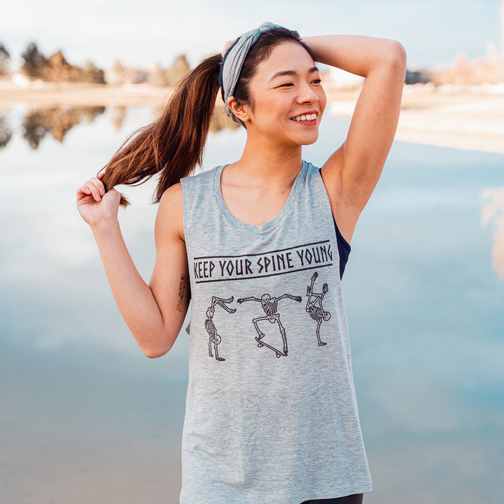 woman wearing a grey muscle tank top with skeletons dancing that says "keep your spine young"