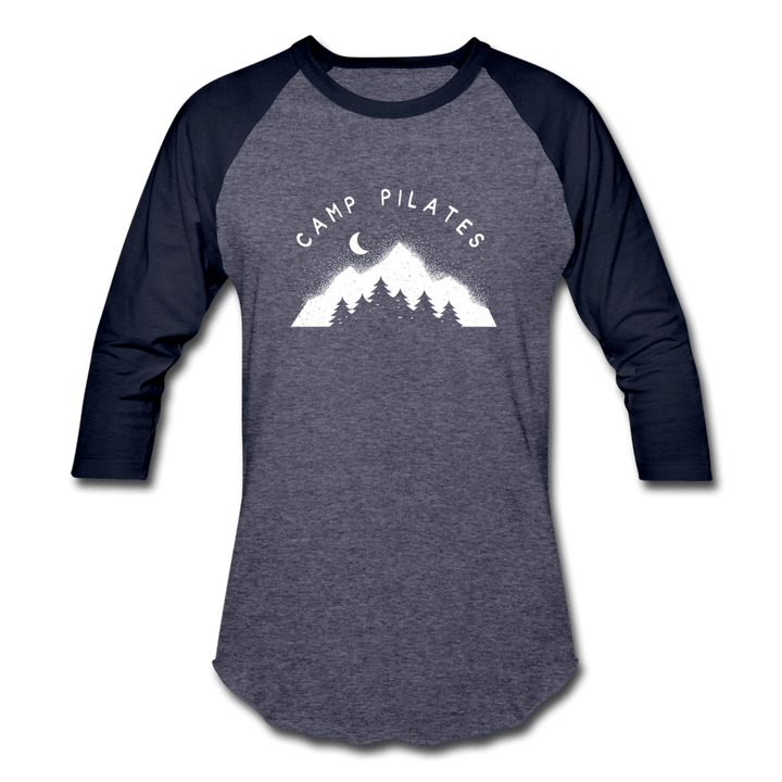 Woman wearing a 3/4 sleeve baseball shirt that says "Camp Pilates" over a mountain design. Both the text and design is in white. 