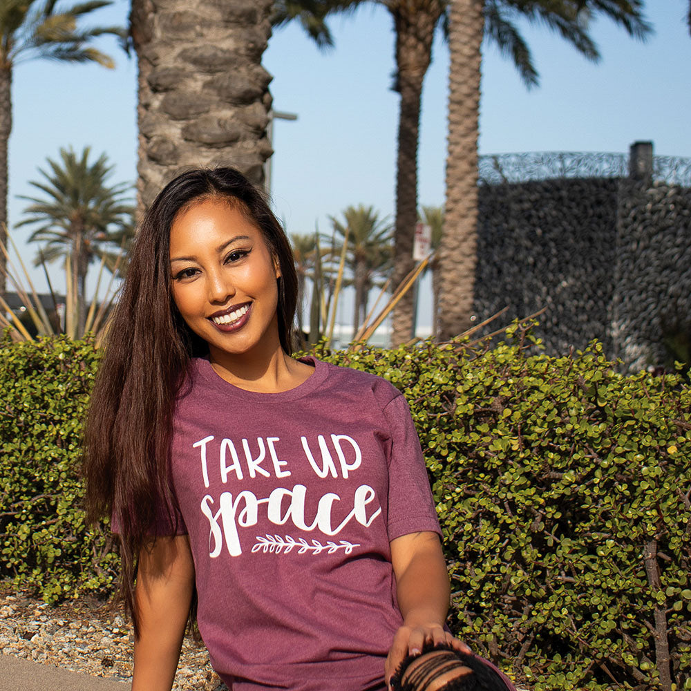 Woman wearing a maroon t-shirt that says "Take Up Space" in white writing 