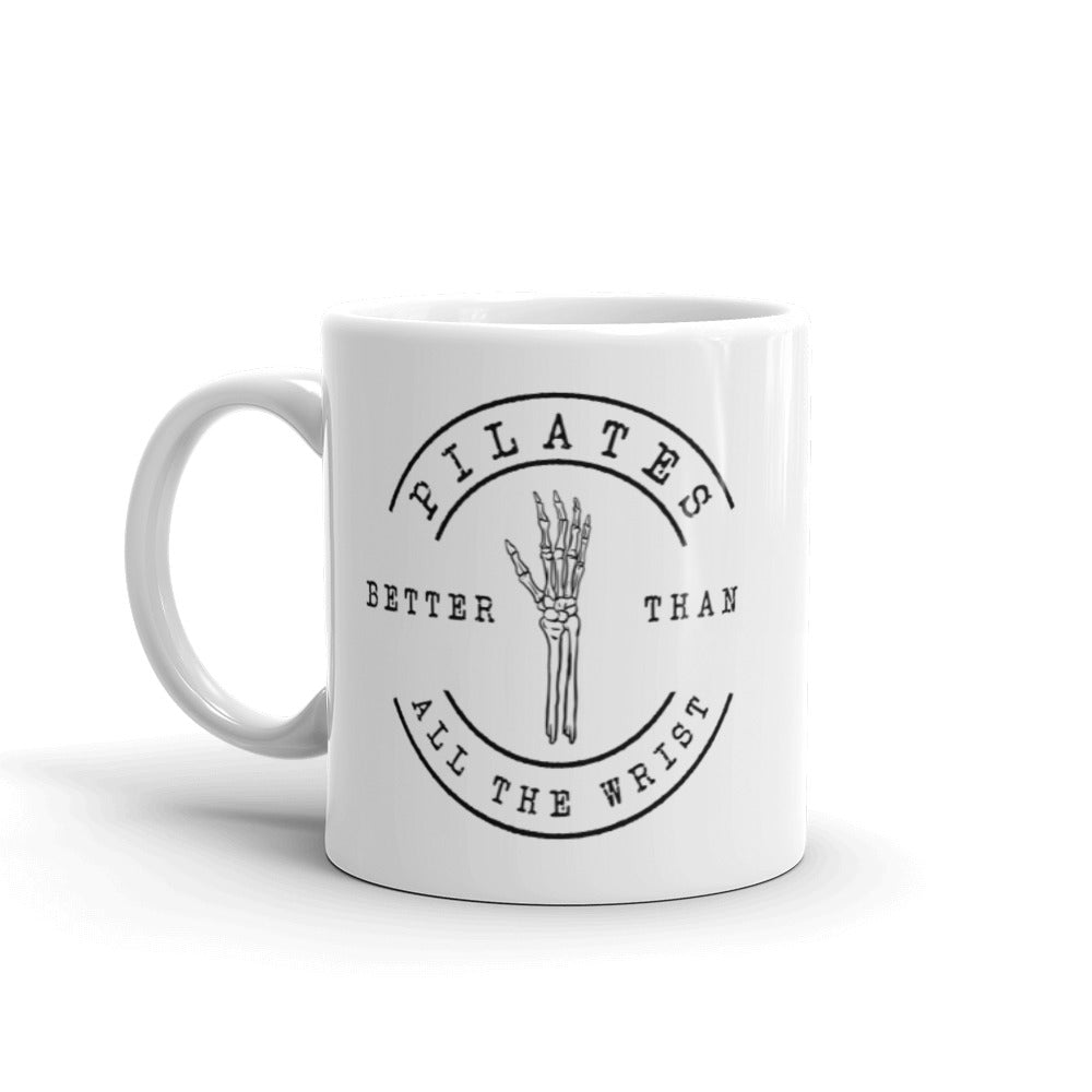 White 11oz mug with handle on the left. The mug says "Pilates Better Than All The Wrist" with a skeleton hand in black text. 