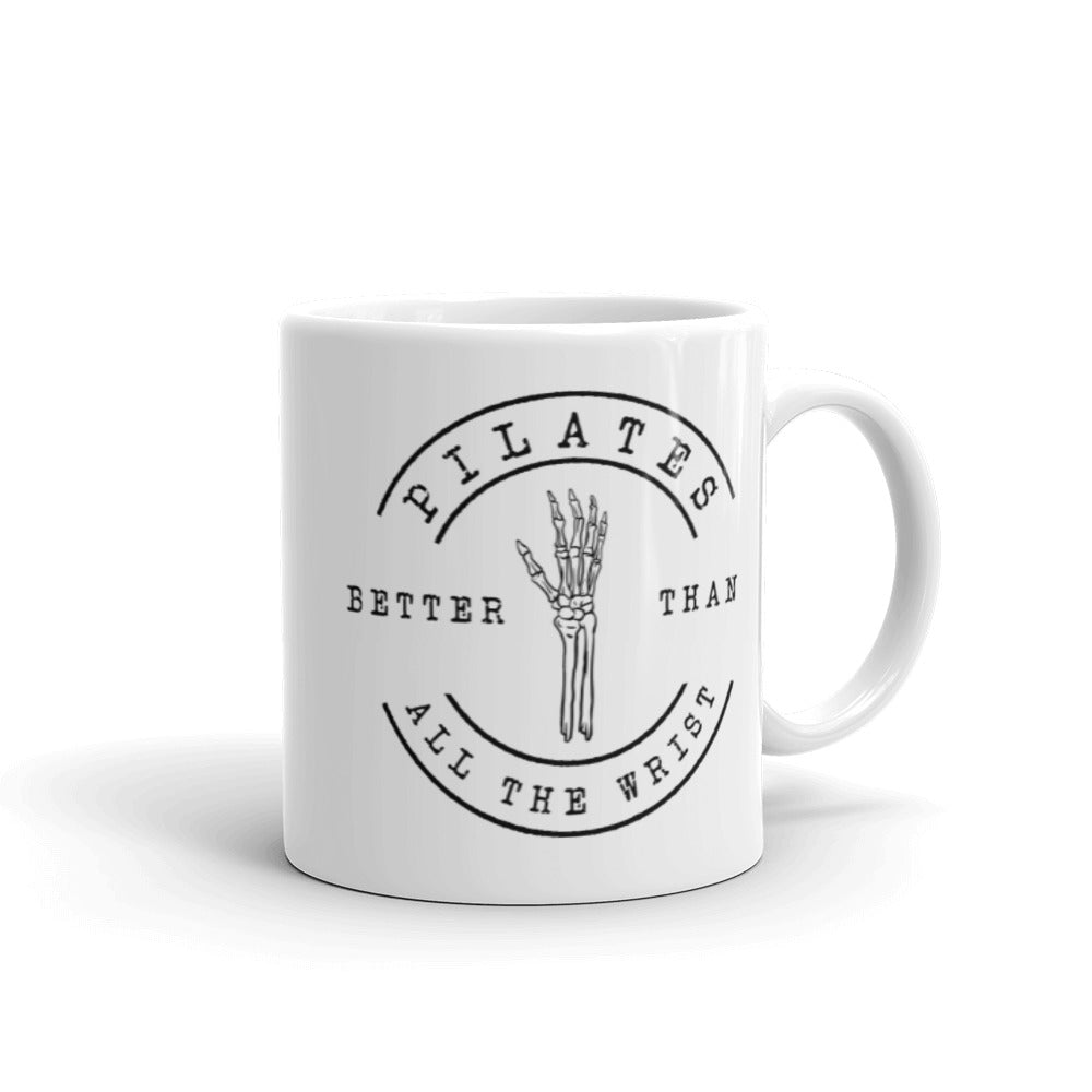 White 11oz mug with handle on the right. The mug says "Pilates Better Than All The Wrist" with a skeleton hand in black text. 