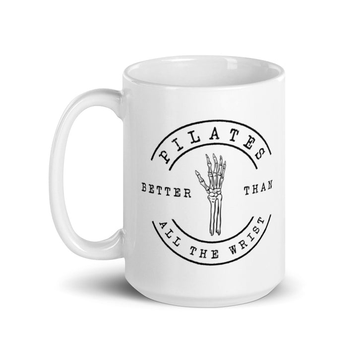 White 15oz mug with handle on the left. The mug says "Pilates Better Than All The Wrist" with a skeleton hand in black text. 
